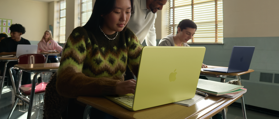 طالبة تستخدم جهاز MacBook Neo بلون أصفر سيتروس، غير موصول بالطاقة داخل قاعة دراسية
