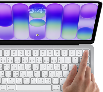 جهاز MacBook Neo، لون فضي، يعرض شاشة تسجيل الدخول، إصبع شخص على مستشعر بصمة الإصبع في الزاوية العلوية اليسرى من لوحة المفاتيح