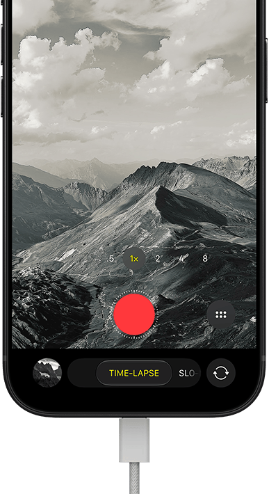 iPhone 18 Pro, front exterior, displaying a mountainous landscape, with the camera mode overlay in Time-Lapse mode, with power cable attached to charging port