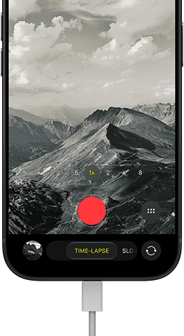 iPhone 18 Pro, front exterior, displaying a mountainous landscape, with the camera mode overlay in Time-Lapse mode, with power cable attached to charging port