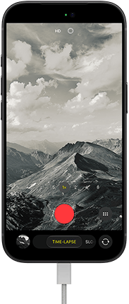 iPhone 18 Pro, front exterior, displaying a mountainous landscape, with the camera mode overlay in Time-Lapse mode, with power cable attached to charging port