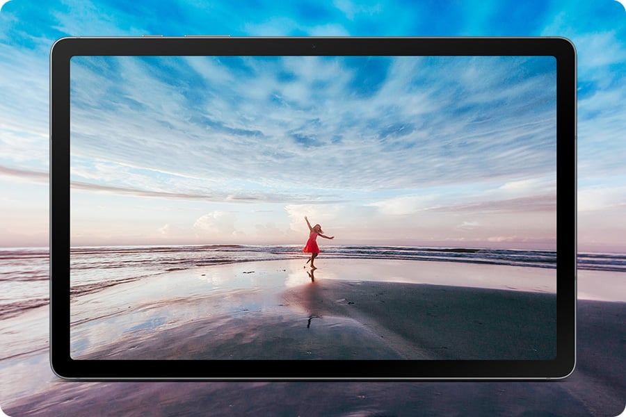 Galaxy Tab S10 Lite displayed horizontally showing a vivid image of a woman in red dress on the beach with arms outstretched against a blue sky and ocean horizon, expressing a free-spirited mood. The expansive scene extends beyond the screen edges, highlighting the large 10.9-inch display and immersive viewing experience that brings content to life.